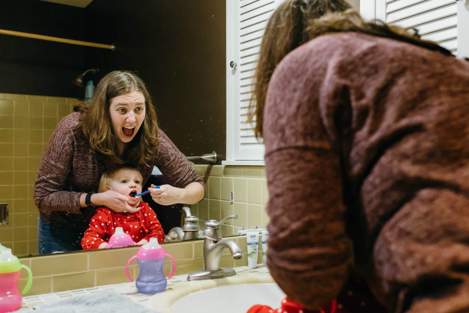 mom helps daughter brush teeth