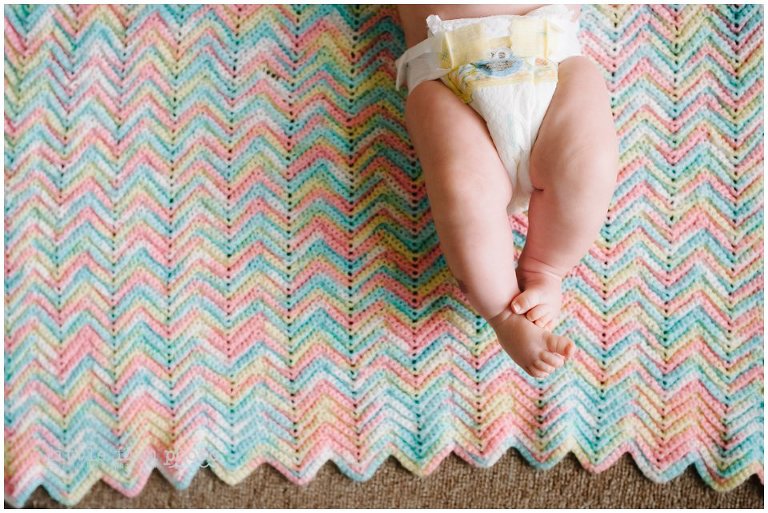 baby rubbing feet together on blue pink and green knit blanket