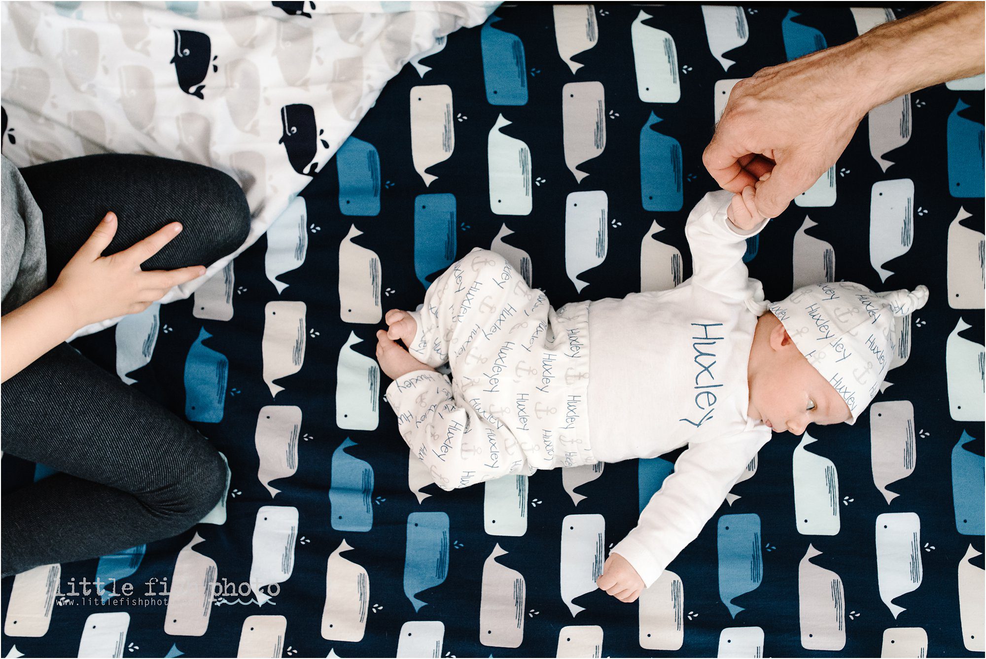 baby in crib while sister sits nearby and father holds hand -