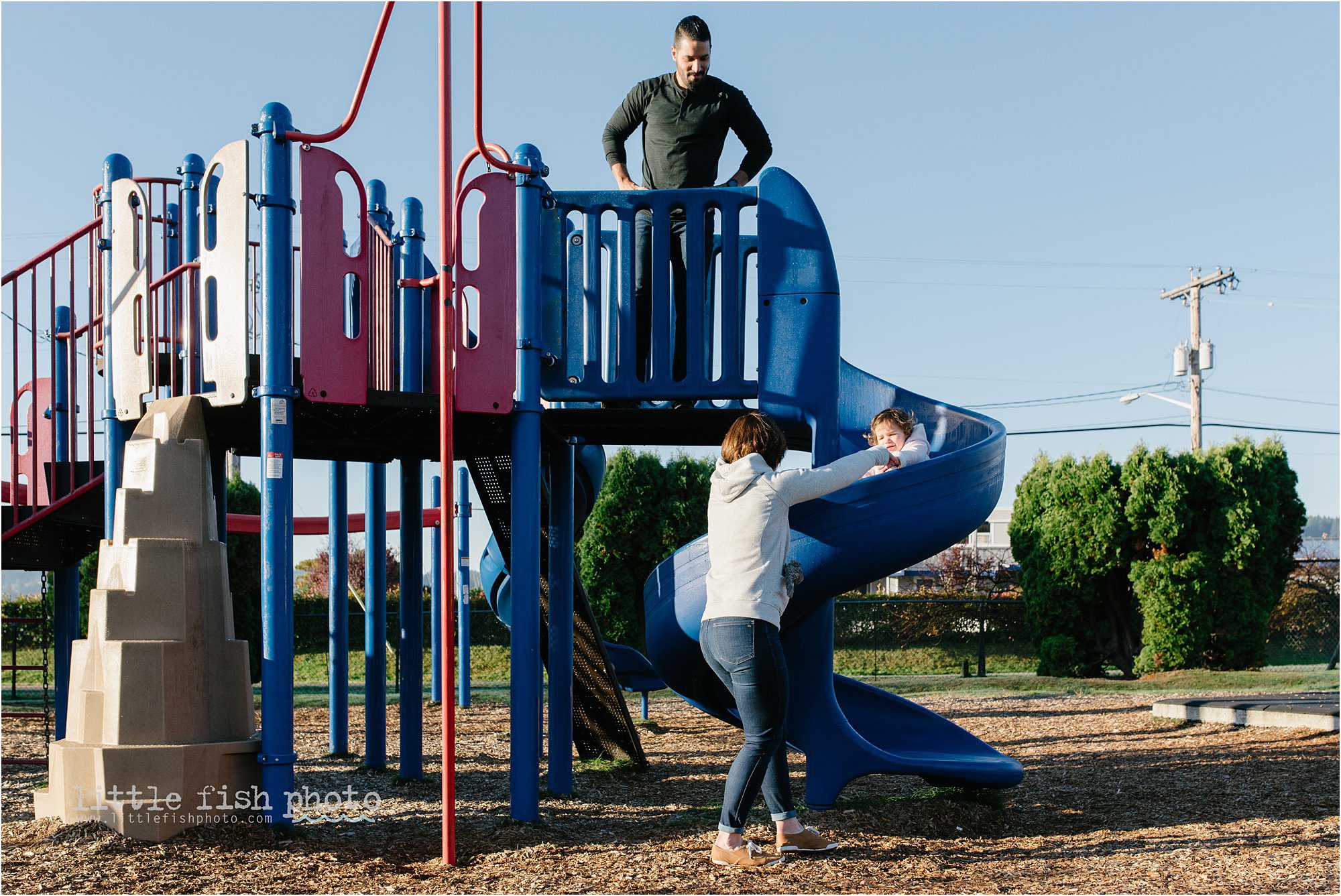 mom helps daughter down slide as father watches on - Kitsap Documentary Family Photographer