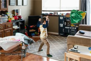 boy throws toy cape on couch - Documentary Family Photography