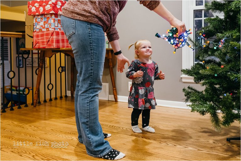 mom helps toddler girl with christmas lights - Kansas City Documentary Family Photographer