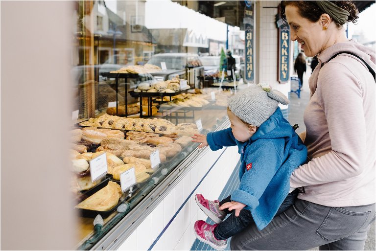 toddler girl reaches for pastries in bakery window