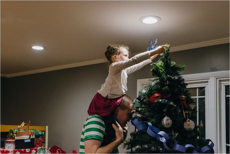 girl puts star on top of Christmas tree - Lifestyle Family Photography