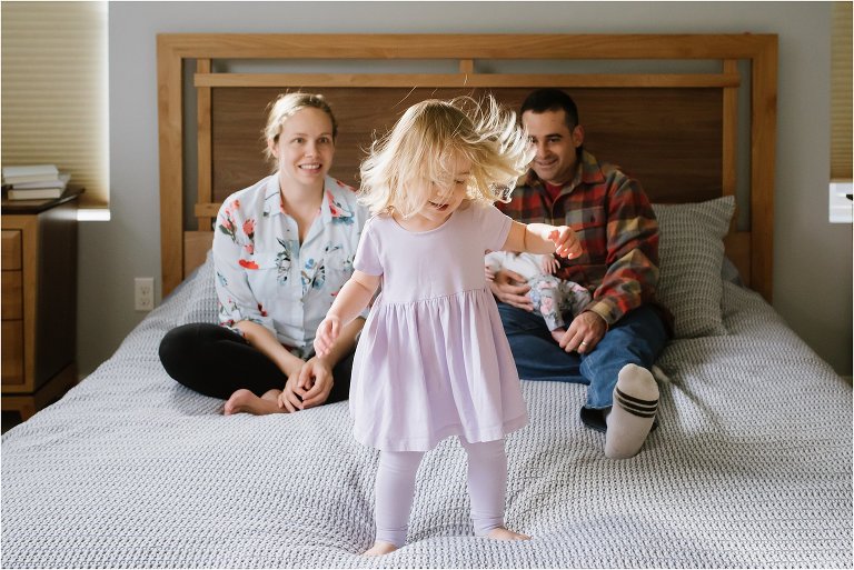 girl jumps on bed in front of family - Poulsbo Lifestyle Newborn Photographer