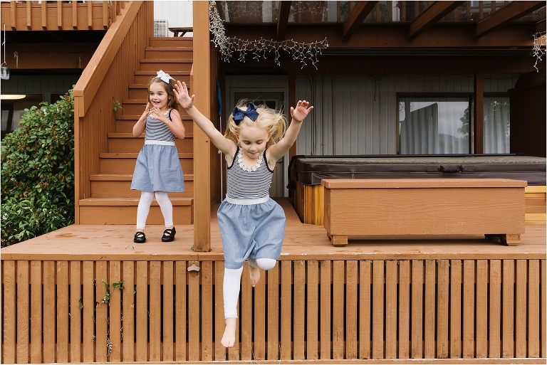Documentary photo of twin girls on porch. One is leaping off the porch the other looks surprised.