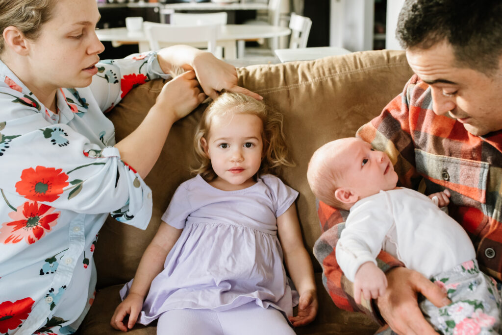 Mom and dad on the couch with a toddler and newborn baby, candid in-home lifestyle family photography in Bremerton
