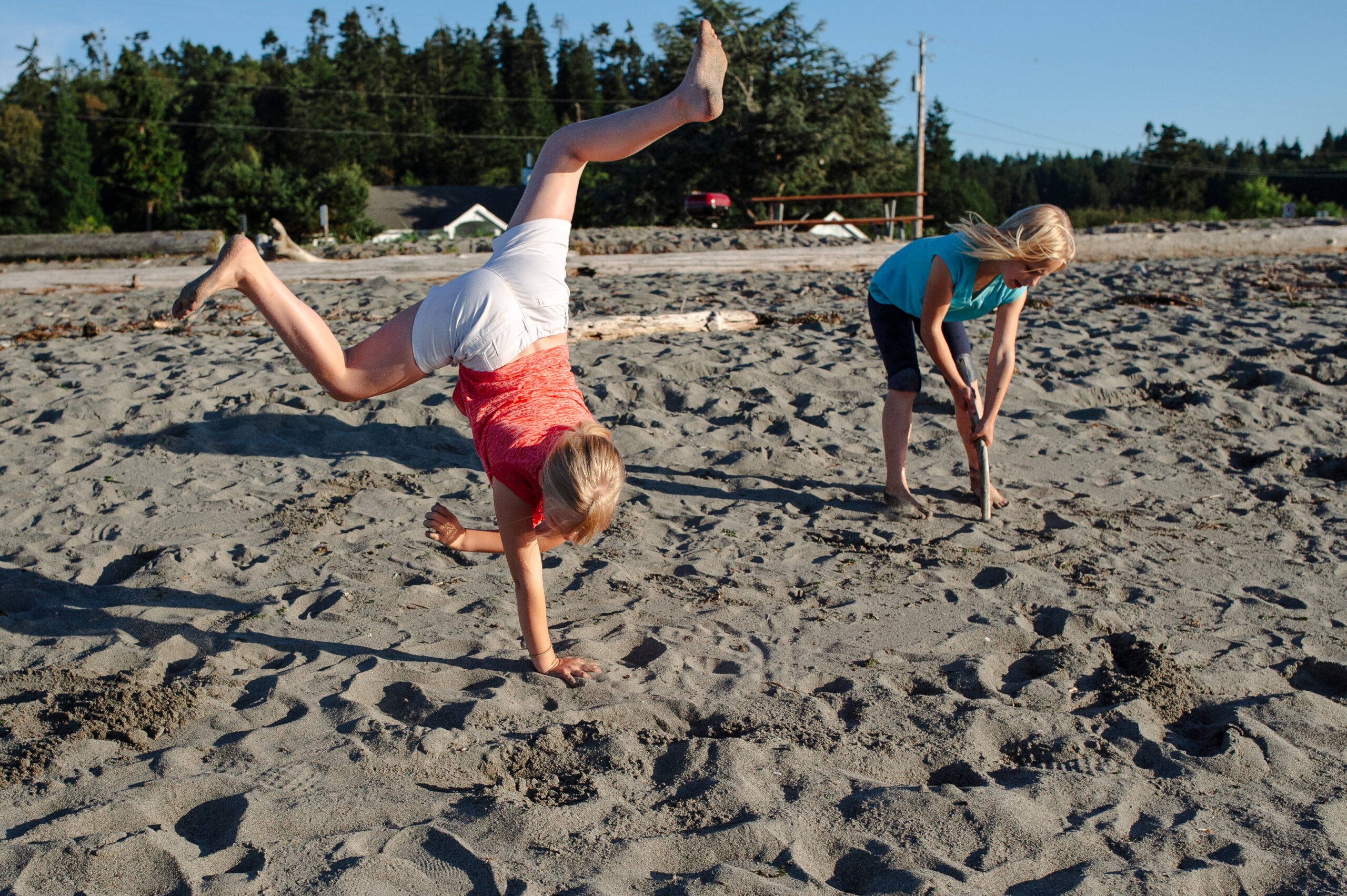 Girl doing a cartwheel on a Kingston beach while her mom looks on, candid outdoor family photography in Kitsap County