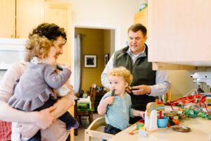 Mom and dad in the kitchen with two toddlers surrounded by toys, candid in-home lifestyle family photography in Kingston