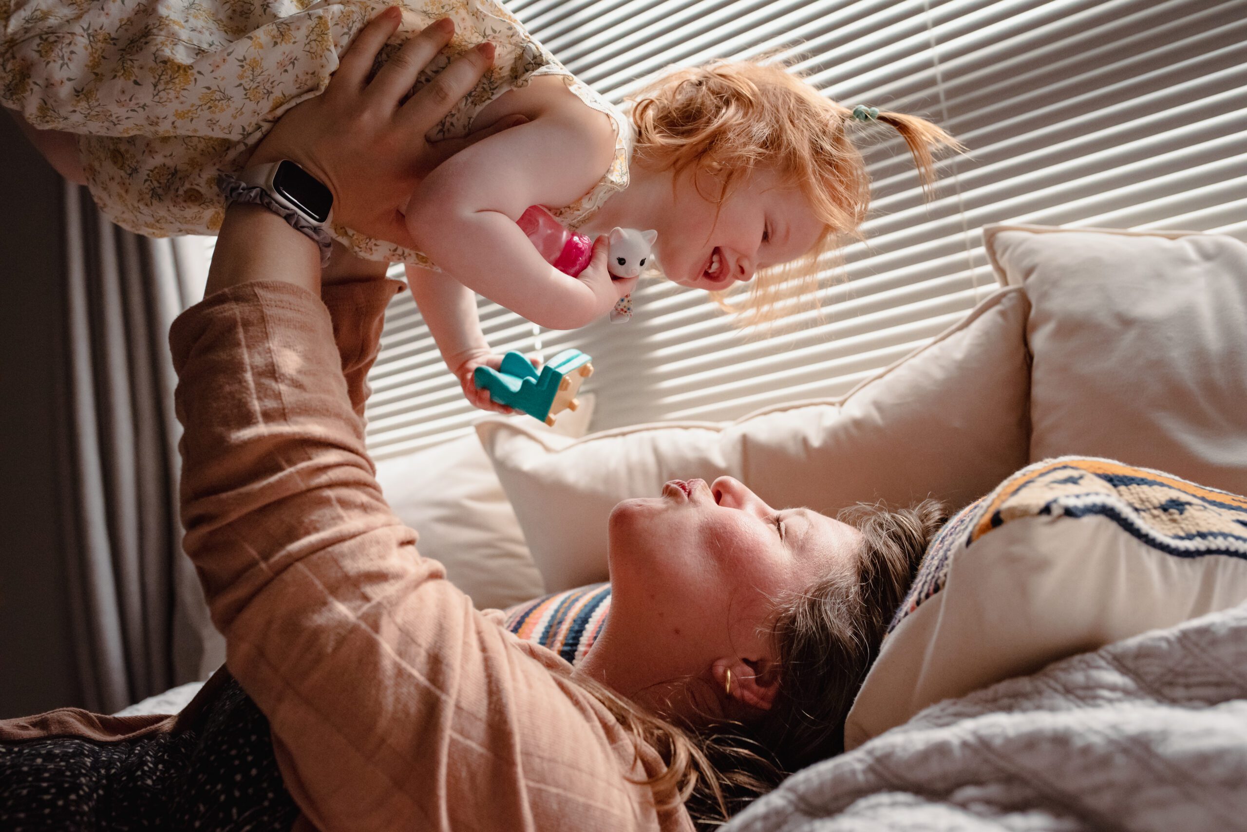 Mom lying on a bed lifting a laughing toddler into the air, candid in-home lifestyle family photography in Silverdale